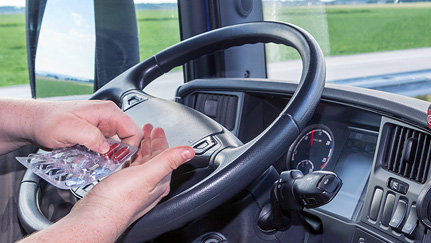 Hand holding medication in front of a steering wheel